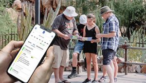 Na imagem, em primeiro plano, há um celular com horários e tela de agendamento online. Ao fundo, uma família se preparando para um passeio de ecoturismo.