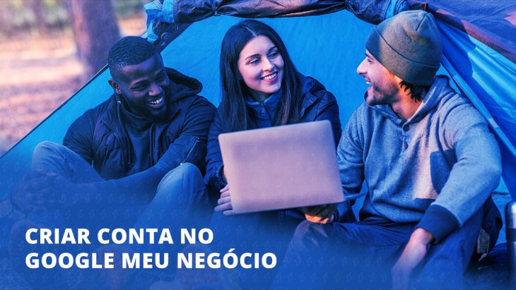 Imagem com três jovens sentados em frente a uma barraca. Um deles está com um notebook na mão e mostrando para os outros.